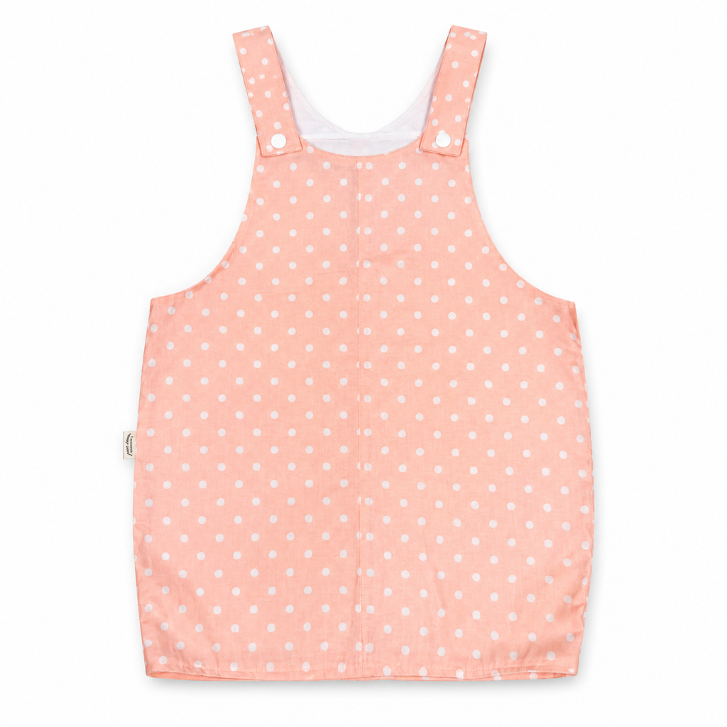 A sleeveless baby romper in a light peach-pink color with a white polka dot pattern, featuring adjustable shoulder straps with snap buttons, shown flat on a white background.