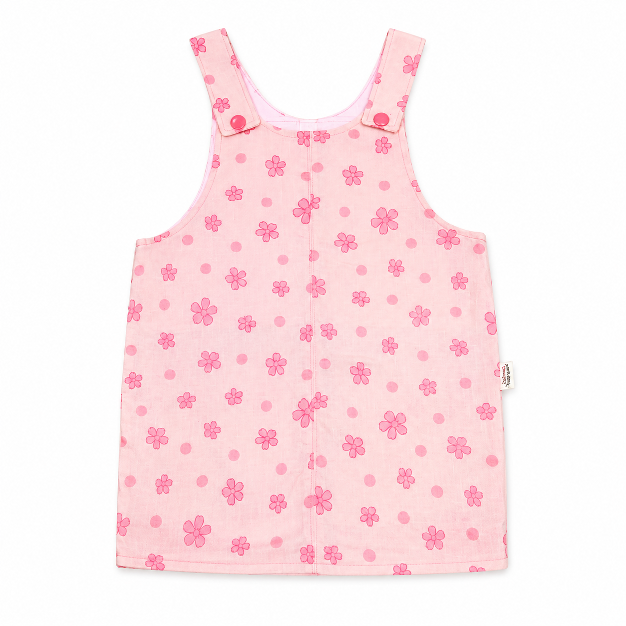 A pink sleeveless baby dress or overall-style romper with a floral and polka-dot pattern, featuring shoulder straps with snap buttons, photographed flat against a white background.