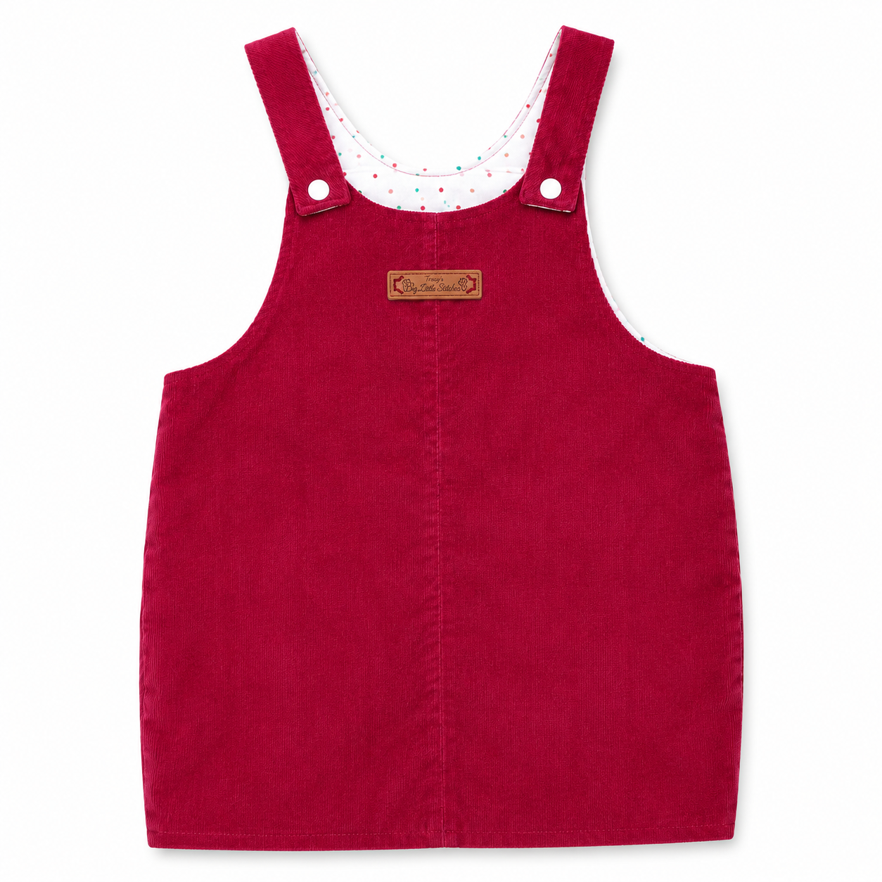 A red corduroy baby overalls dress with adjustable shoulder straps, a white inner collar with colorful polka dots, and a small brown leather brand patch on the chest.