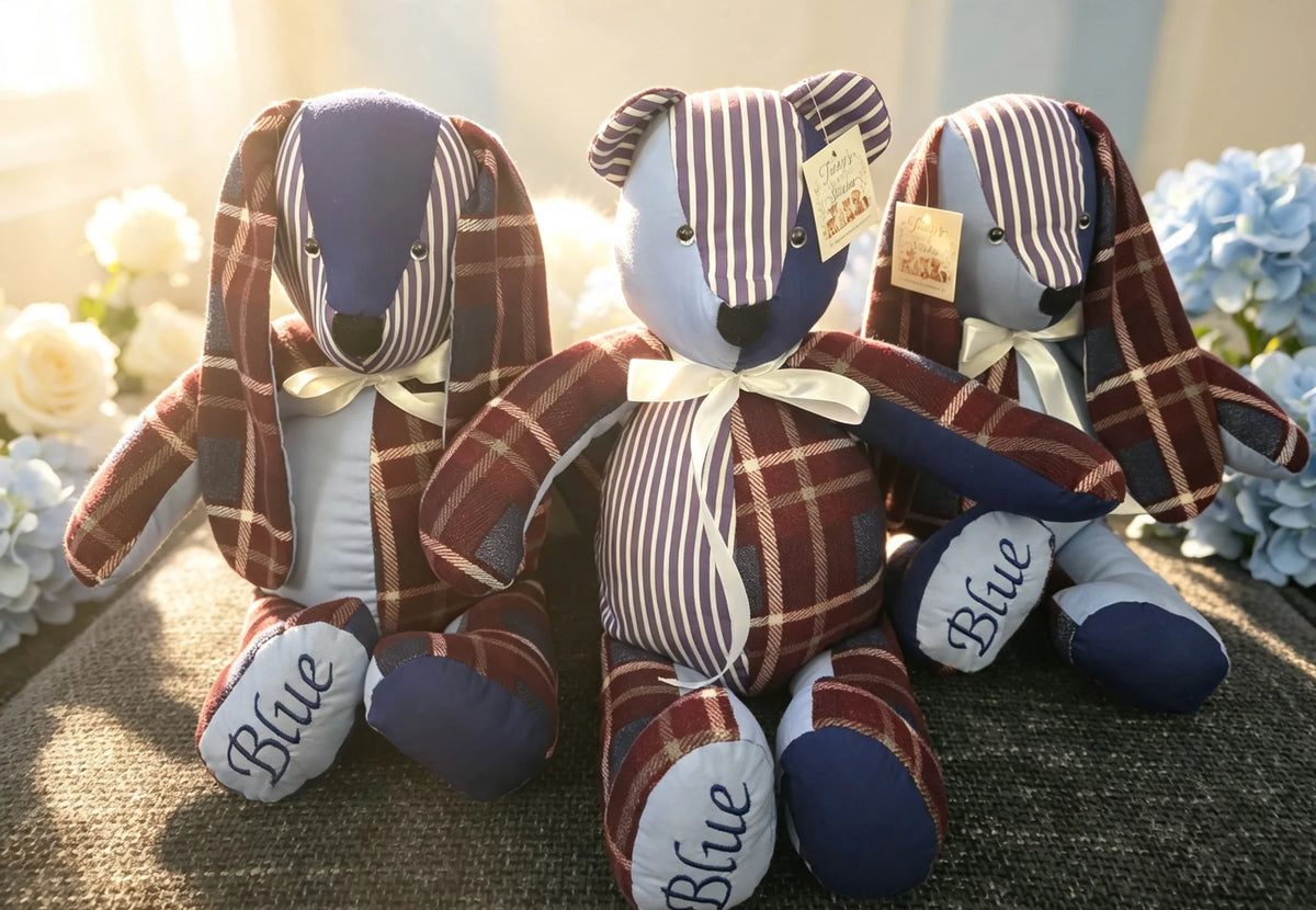 Three handmade plush teddy bears dressed in matching plaid and striped outfits, sitting together on a textured surface with white and blue flowers in the background.